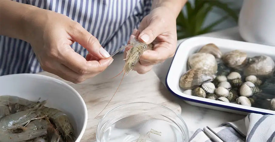 Cómo limpiar marisco en casa: manos femeninas desvenando una gamba fresca sobre una tabla de cocina