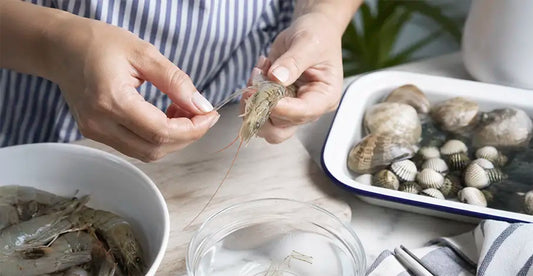 Cómo limpiar marisco en casa: manos femeninas desvenando una gamba fresca sobre una tabla de cocina